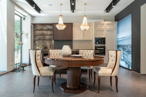 Interior of elegant spacious kitchen with wooden furniture and shiny crystal chandelier hanging over dining zone with round table and comfortable chairs