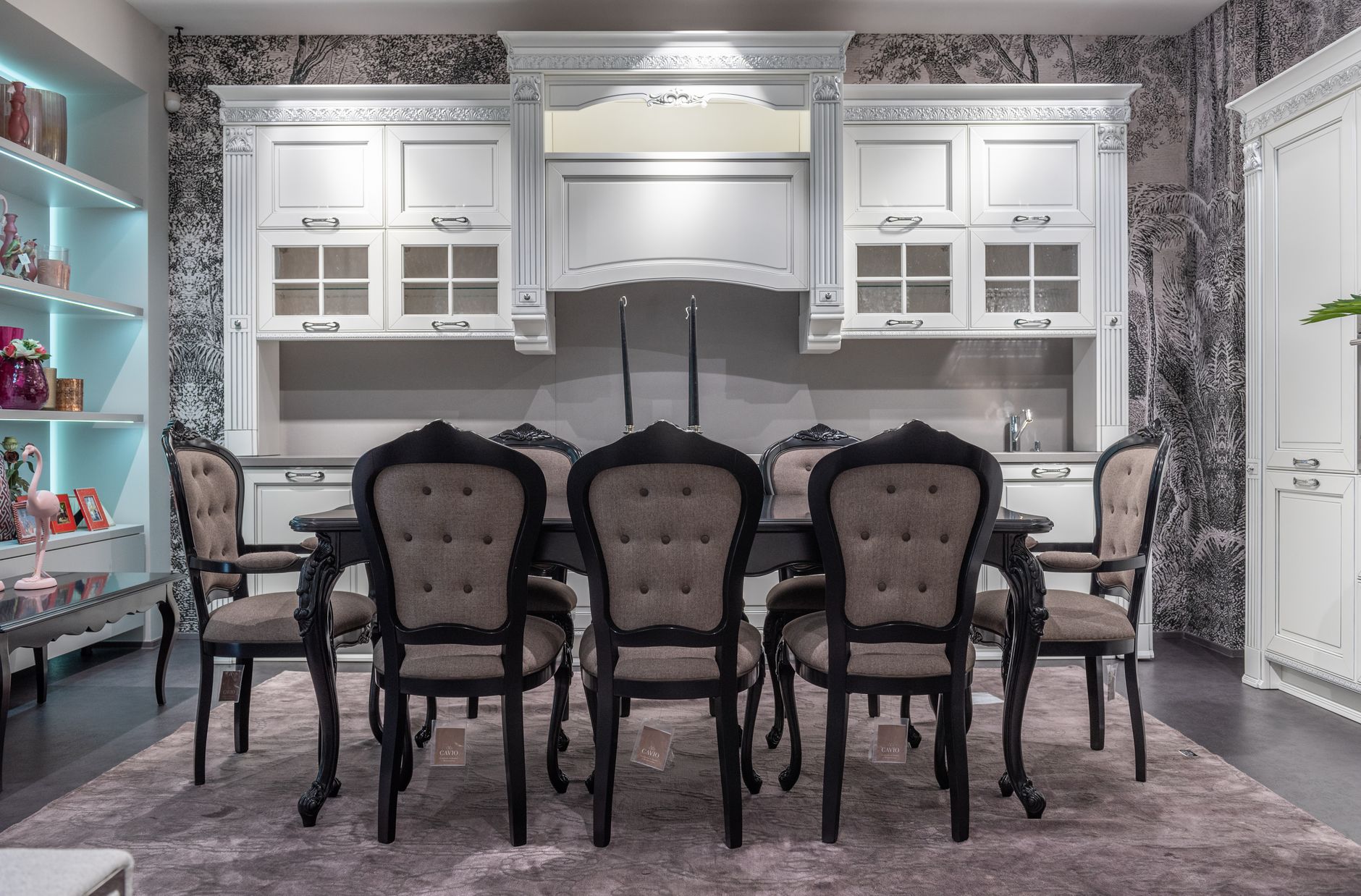 Comfortable chair and big dining table placed in classic styled kitchen with white furniture near illuminated shelves with various decorative items