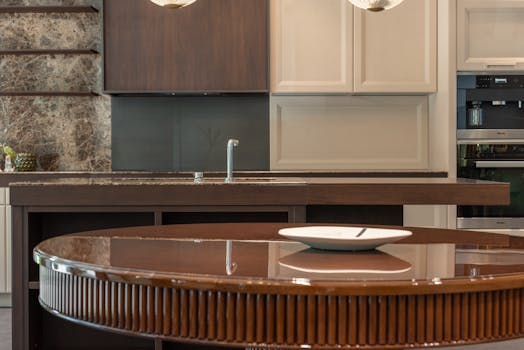 White ceramic plate placed on round brown dining table with shiny surface in elegant kitchen with wooden cabinets and modern appliances