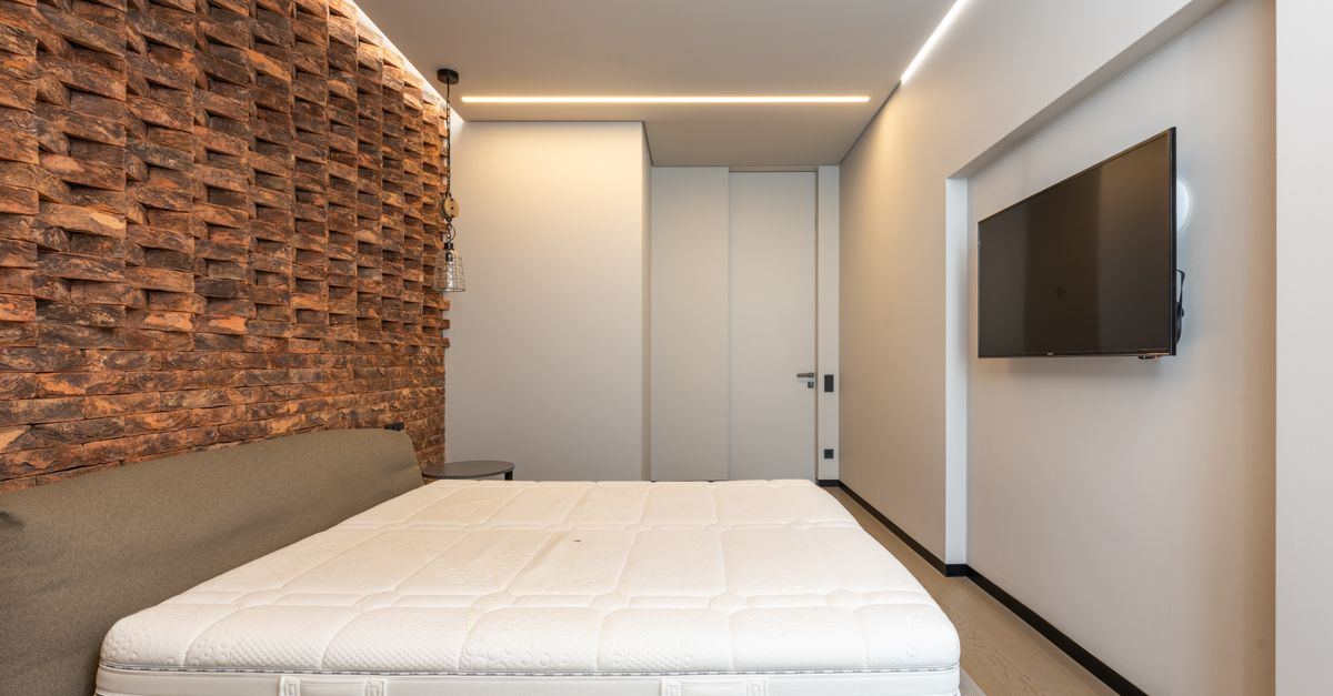Comfortable be with soft mattress in stylish minimalist bedroom with modern TV and creative brick wall