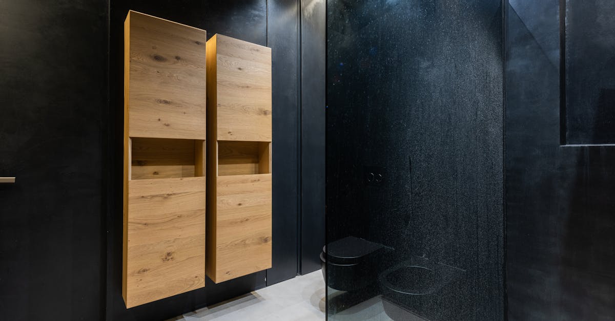 Wooden cupboards hanging on black wall near toilet bowl and shower cabin in contemporary bathroom
