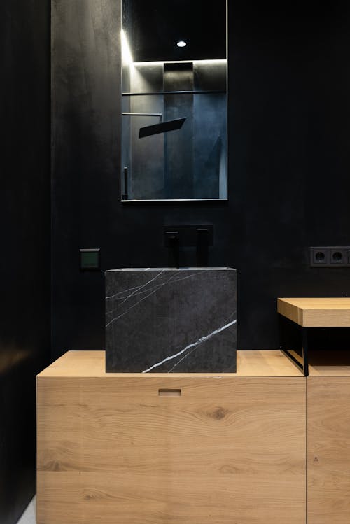 Free Interior details of modern bathroom with square black marble sink placed on wooden cabinet under mirror hanging on wall Stock Photo