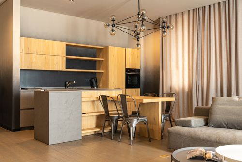 Free Comfortable couch placed near wooden table with chairs in stylish kitchen with cupboards in modern apartment with curtains and chandelier Stock Photo