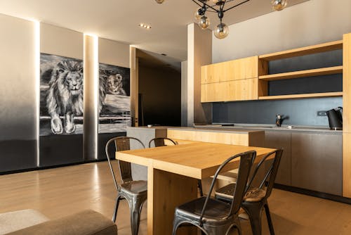 Wooden table with chairs placed in kitchen with cupboards and shelves in stylish spacious apartment with picture of lion at home