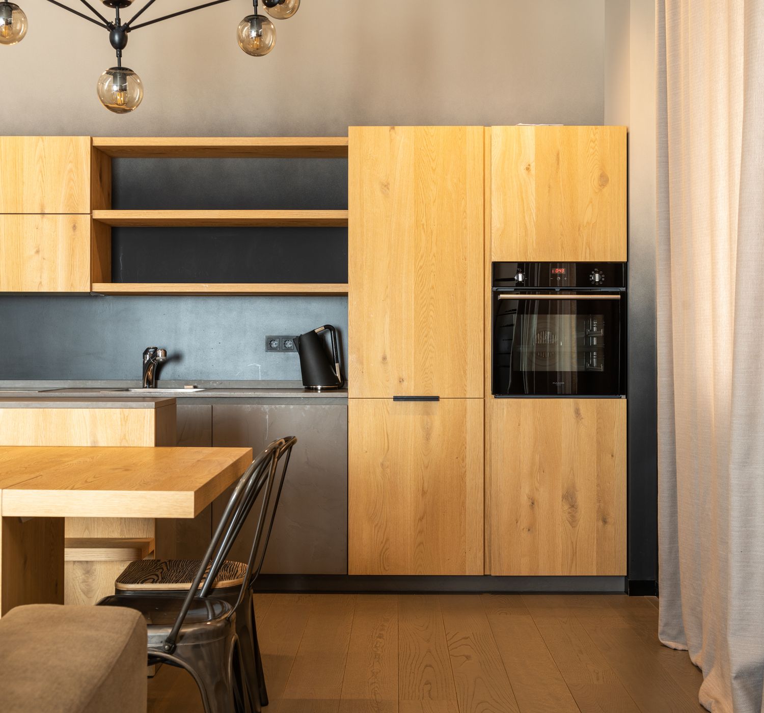 Wooden table with chairs placed in stylish kitchen with cupboards and modern appliances in