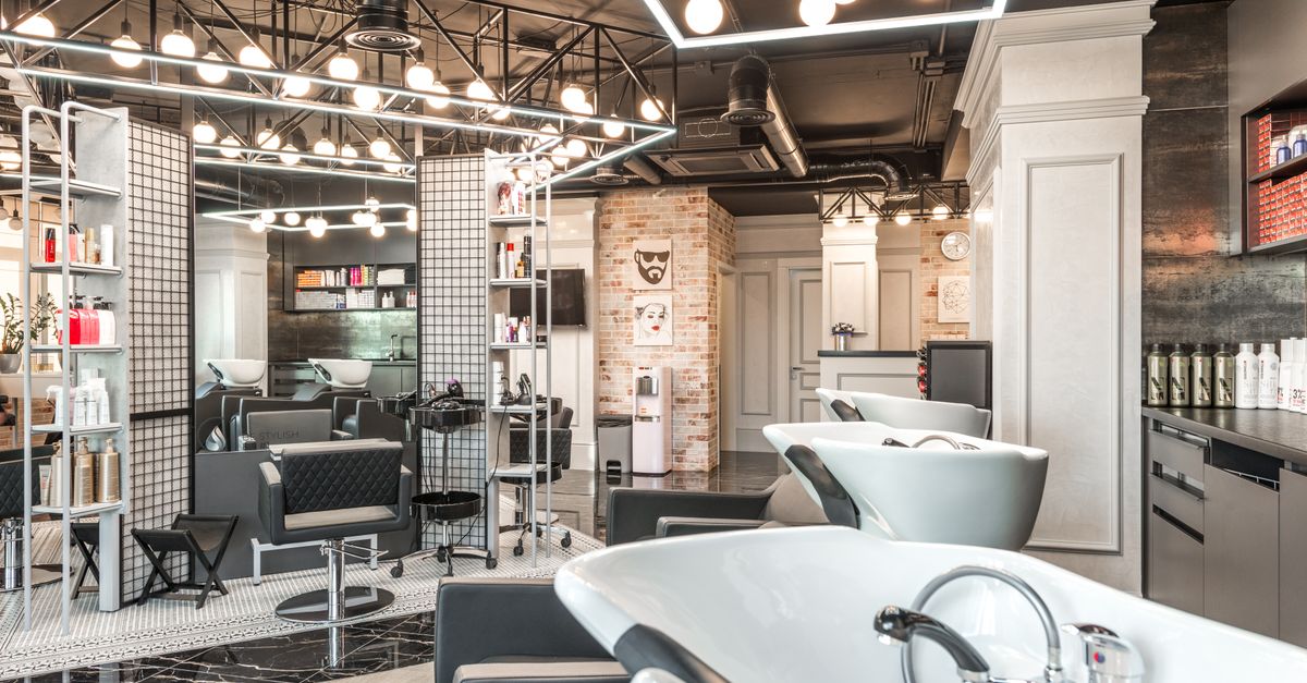 Backwash chairs with sinks placed in stylish spacious beauty salon with mirror and various cosmetology products under bright glowing lamps