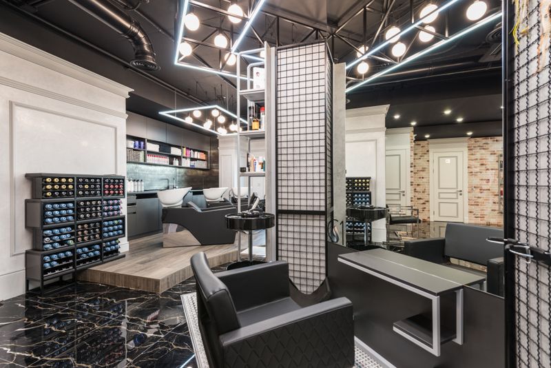 Black leather chair placed against mirror with reflection in stylish beauty salon with backwash chairs and abundance of cosmetology products