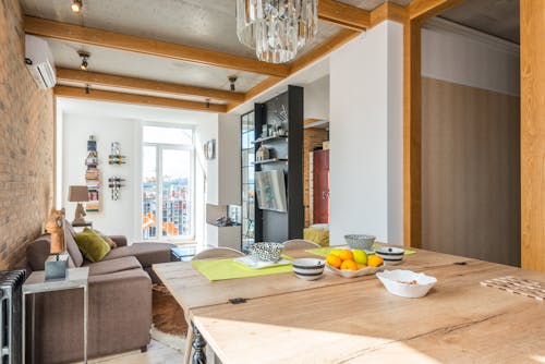 Dishware served on table with fruits near living room with couch placed against wall with TV in modern stylish apartment