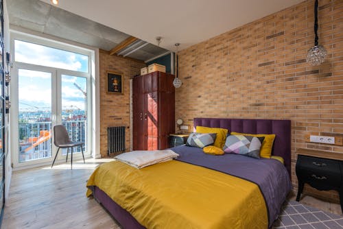 Free Purple and Yellow Bed Beside a Brown Brick Wall Stock Photo