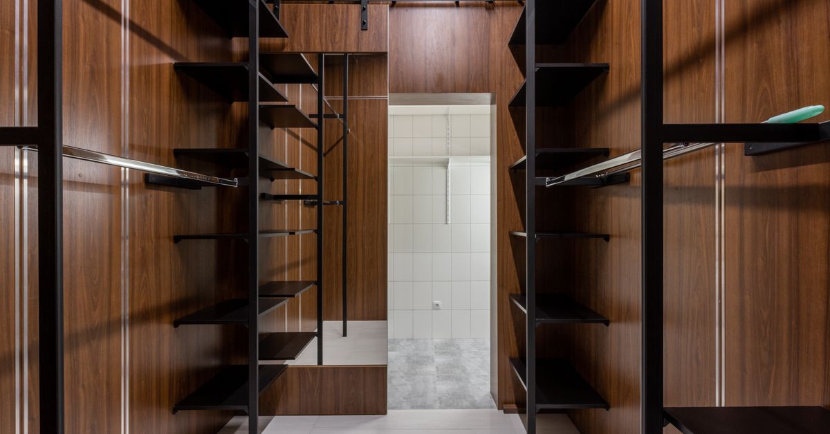 Empty black shelves and racks placed in modern walk in closet with brown walls and mirror with reflection at home