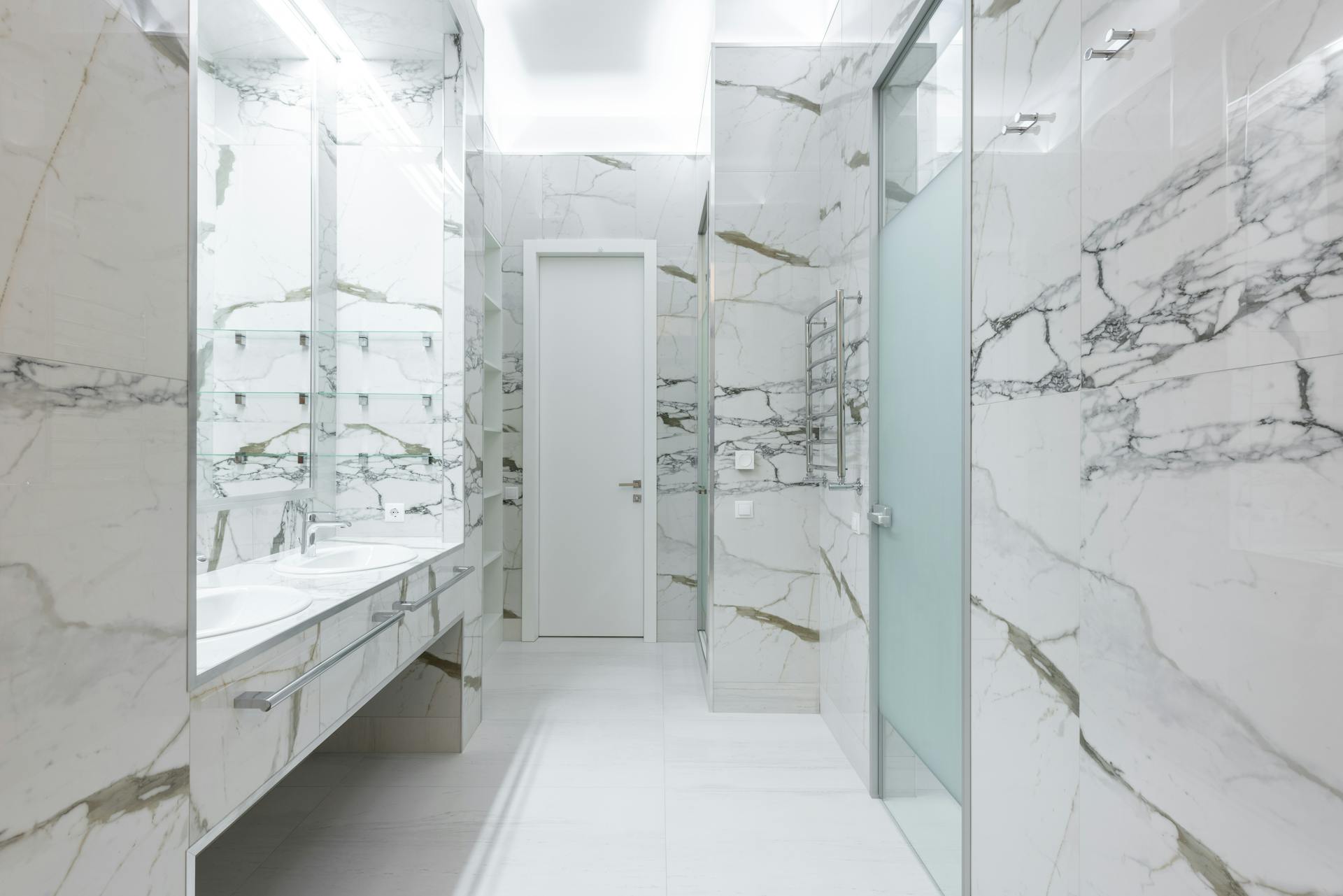 White sinks with taps placed on cabinet at wall in light contemporary bathroom with doors and bright illumination at home