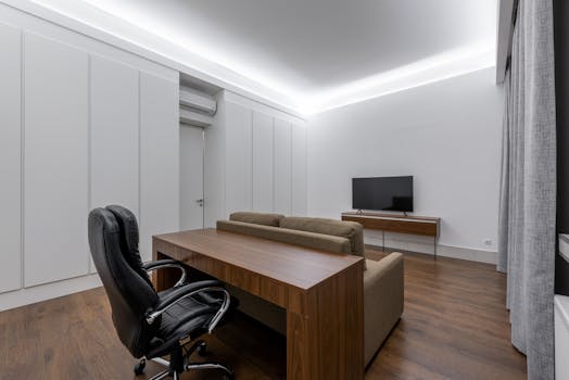 Armchair at wooden table placed near comfortable couch against modern TV in spacious living room with closed door and curtains