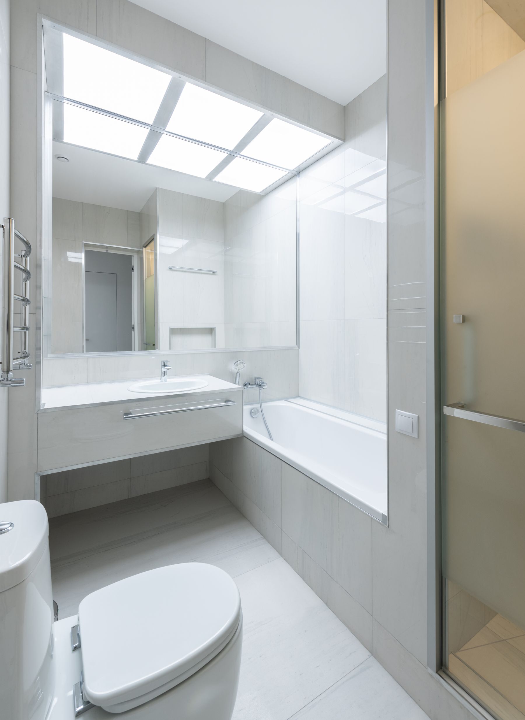 Bright modern bathroom with white bathtub, sink, toilet and illuminated mirror