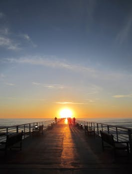 People walking on a pier at sunset with a vibrant sky and ocean view.
