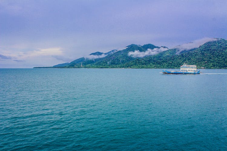 Blue And White Yacht On Teal Sea Near Green Mountain