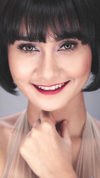 Elegant close-up portrait of a smiling young woman with bangs, showcasing a modern hairstyle and makeup.