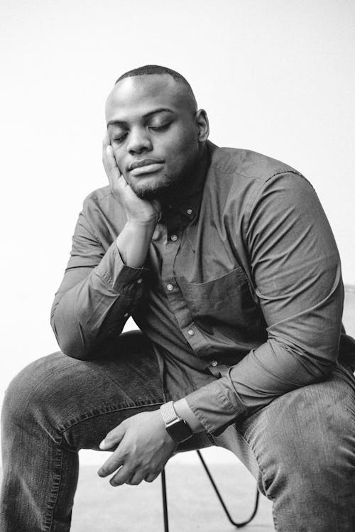 A Man in Long Sleeve and  Denim Jeans Sitting on a Chair