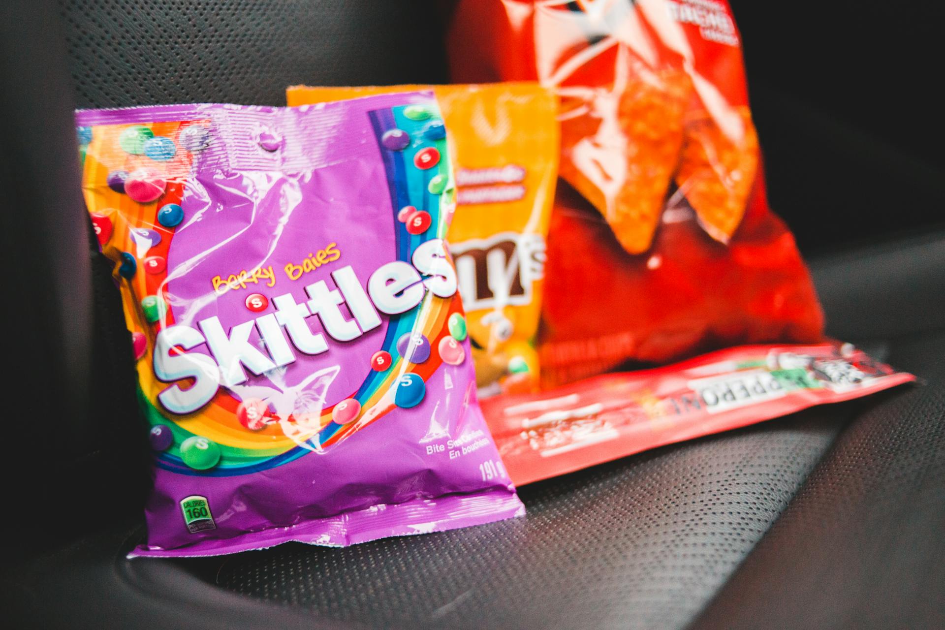 Closeup composition of multicolored packages with tasty treats placed in row on dark seat of car