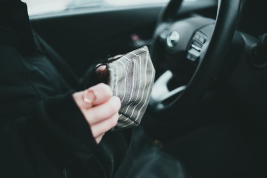 Crop anonymous female in black outerwear with ring holding protective mask while sitting in car