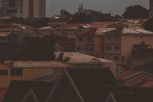 Free A dark, moody view of urban rooftops with a warm sunset glow highlighting the residential area. Stock Photo
