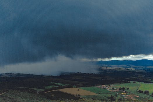 Aerial photograph showcasing sprawling fields and distant mountains beneath ominous rain clouds.