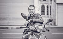 一名年轻人坐在滑板车上，在城市街道上微笑