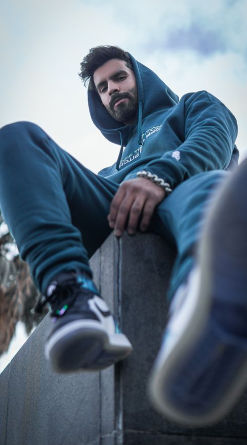 Free Bearded man in hoodie and sneakers sitting on concrete in Fes, showing urban style. Stock Photo
