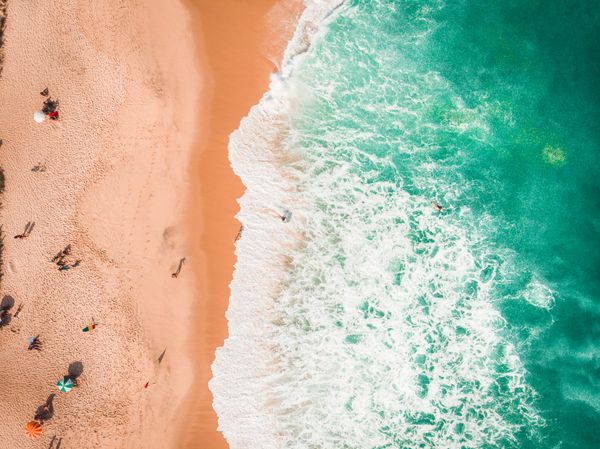 Imagem de drone capturando a vibrante cena da praia do Rio de Janeiro com ondas turquesa e areia dourada.