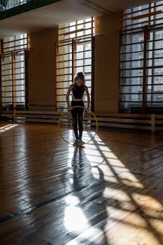 A girl using a plastic hoop for exercise in a gym with dramatic lighting and shadows.