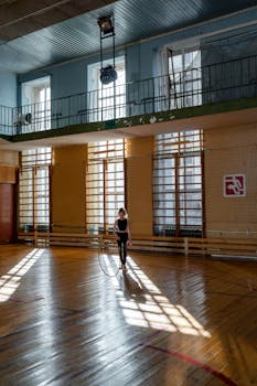 Girl performing gymnastics with a hula hoop in a sunlit indoor gymnasium.