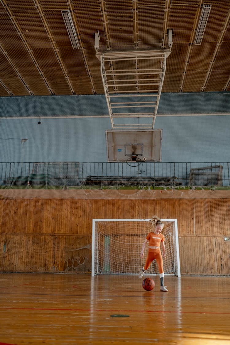 A Young Girl  In Orange Shirt Playing A Basketball