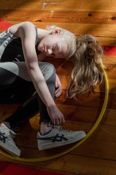 Caucasian girl lying indoors on wooden floor with hula hoop, in sportswear.