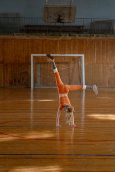 A young girl in orange attire performs a cartwheel on a gymnasium floor, showcasing her gymnastics skills.