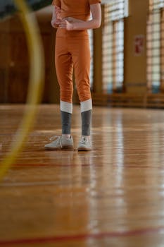 Close-up of an athlete in orange sportswear standing indoors with a hula hoop, showcasing fitness activity.