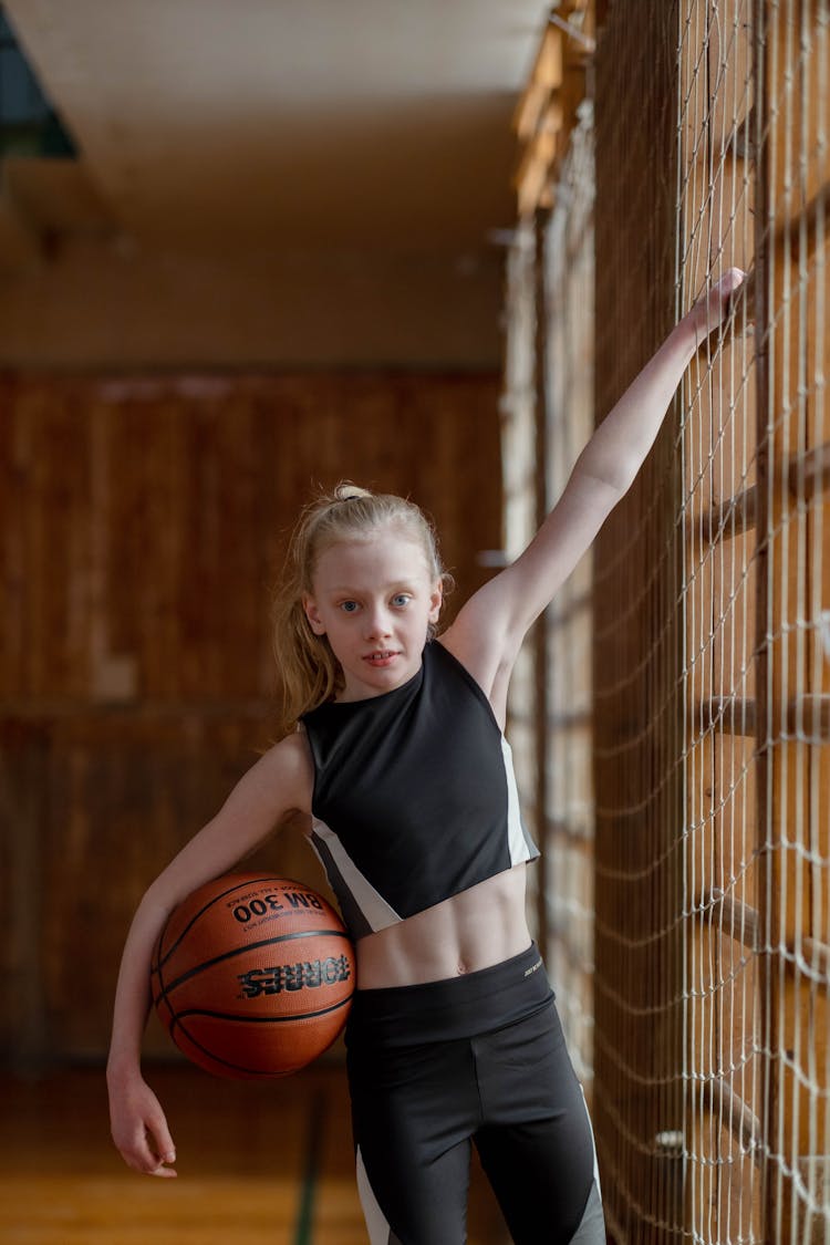 A Girl Holding Onto A  Net And Basketball