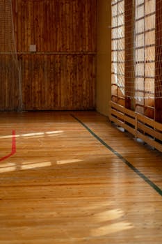 Empty gymnasium with polished wooden floor and sunlit walls, ideal for sports.