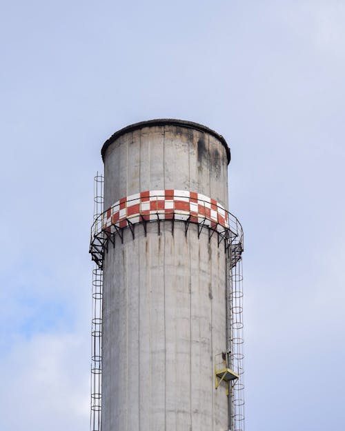 Industrial chimney with staircases under cloudy sky in town