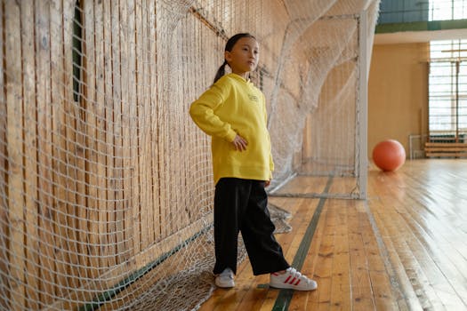 A young girl in a yellow jacket poses in a gym, showcasing sportswear fashion.