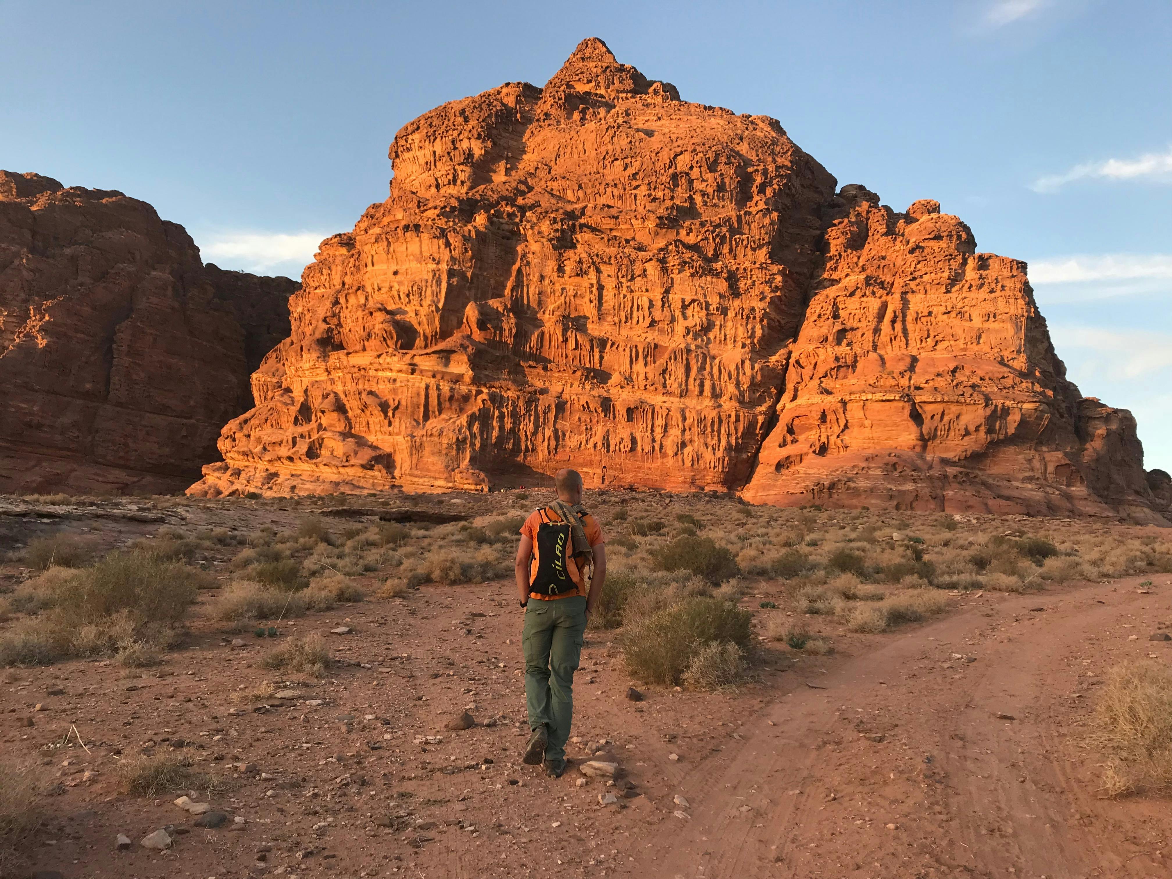 一位孤独的冒险家徒步前往偏远沙漠中引人注目的红色砂岩悬崖，捕捉冒险与孤独的本质