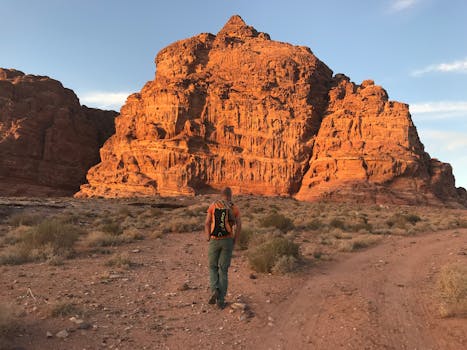 一位孤独的冒险家徒步前往偏远沙漠中引人注目的红色砂岩悬崖，捕捉冒险与孤独的本质