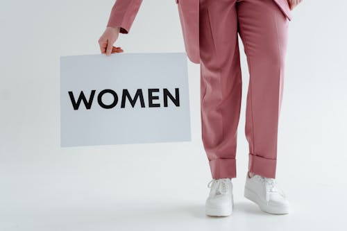 Free A Person in Pink Pants and White Shoes Standing on a White Surface wile Holding a White Paper Stock Photo