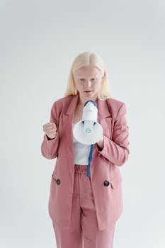 Strong woman wearing pink blazer holding a megaphone on a white background.