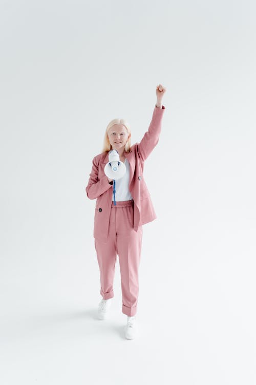 A Woman in Pink Blazer and Pants Talking while Holding a Megaphone