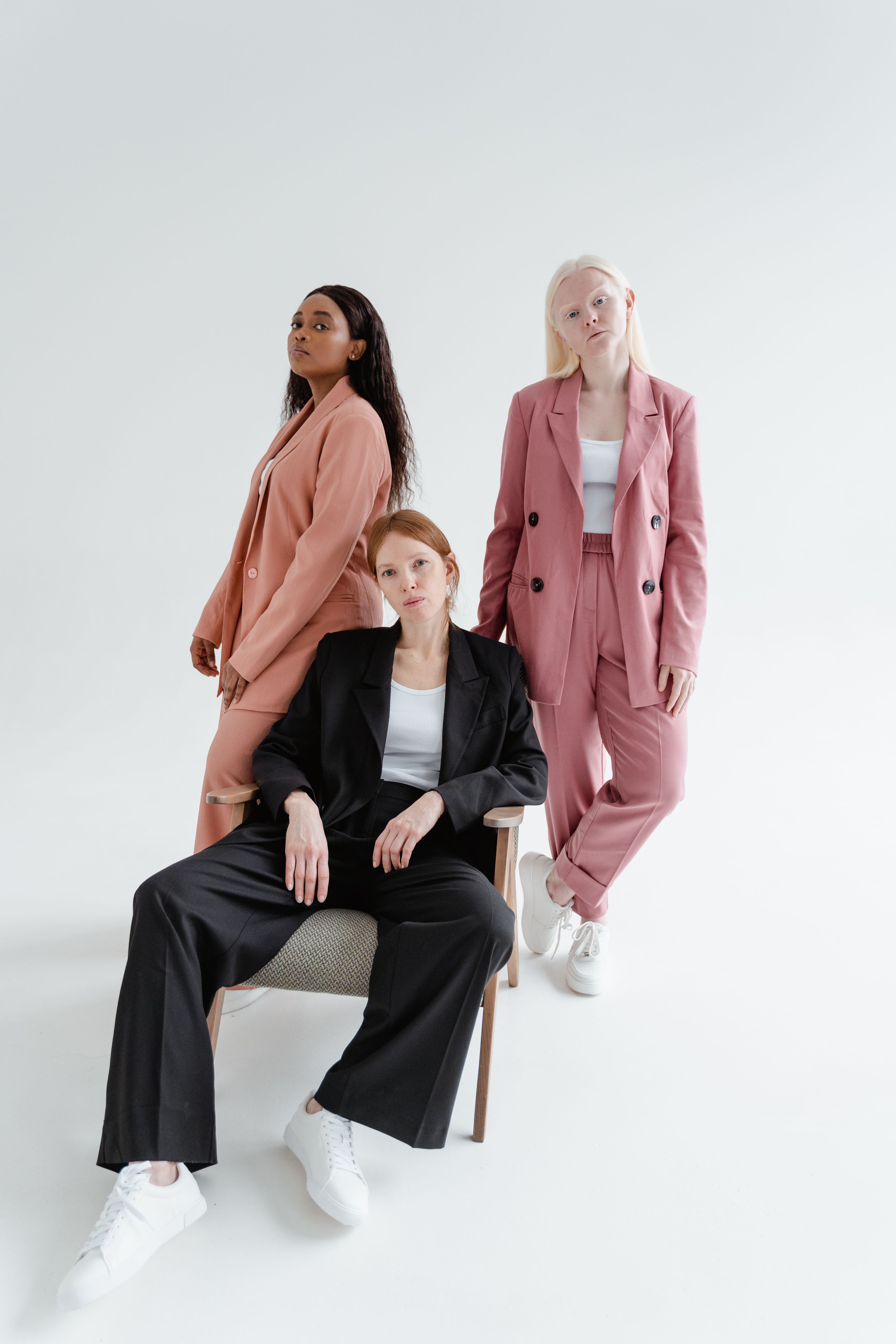 Três mulheres elegantes em blazers posando com confiança em um estúdio brilhante.