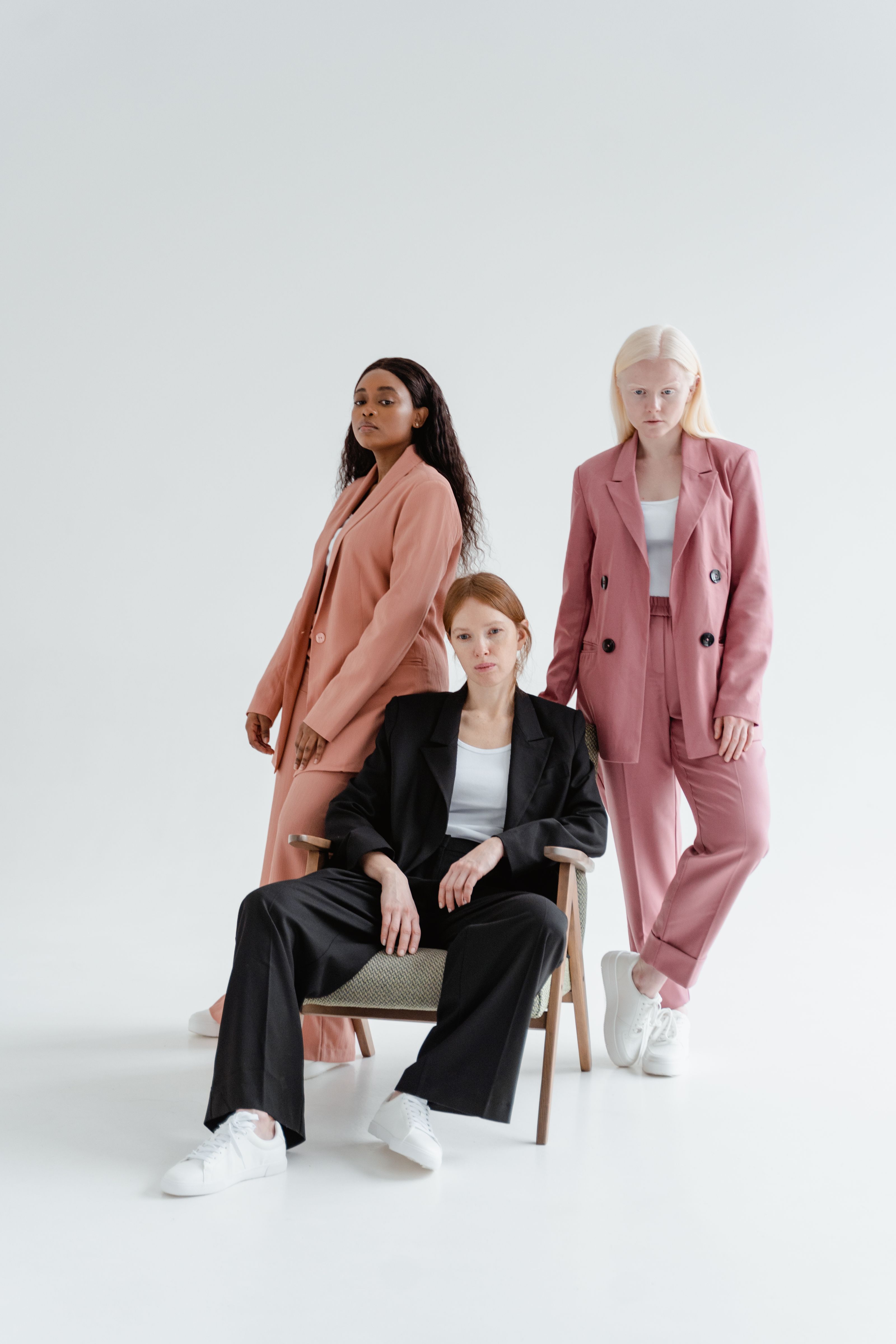 Um grupo diversificado de mulheres posando em trajes elegantes em um ambiente de estúdio, mostrando roupas de negócios modernas.