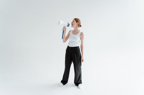 Free A Woman in White Tank Top and Black Pants Holding a Megaphone Stock Photo