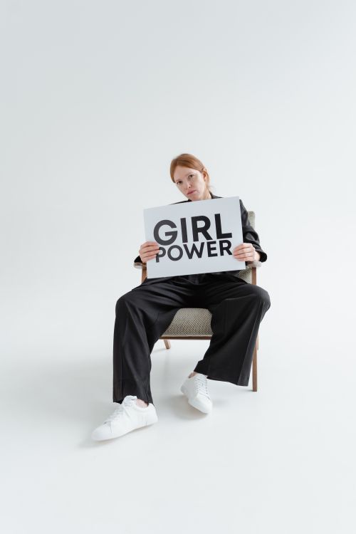 Free Confident woman in black suit holding 'Girl Power' placard, sitting in a chair in a studio. Stock Photo