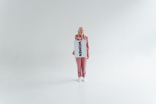 Free A woman in a pink suit holds a 'Women' sign, symbolizing empowerment in a minimalist studio. Stock Photo