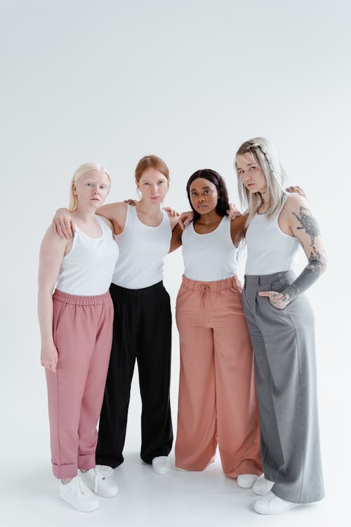 Women Standing Next to Each Other Wearing White Tank Top and Pants