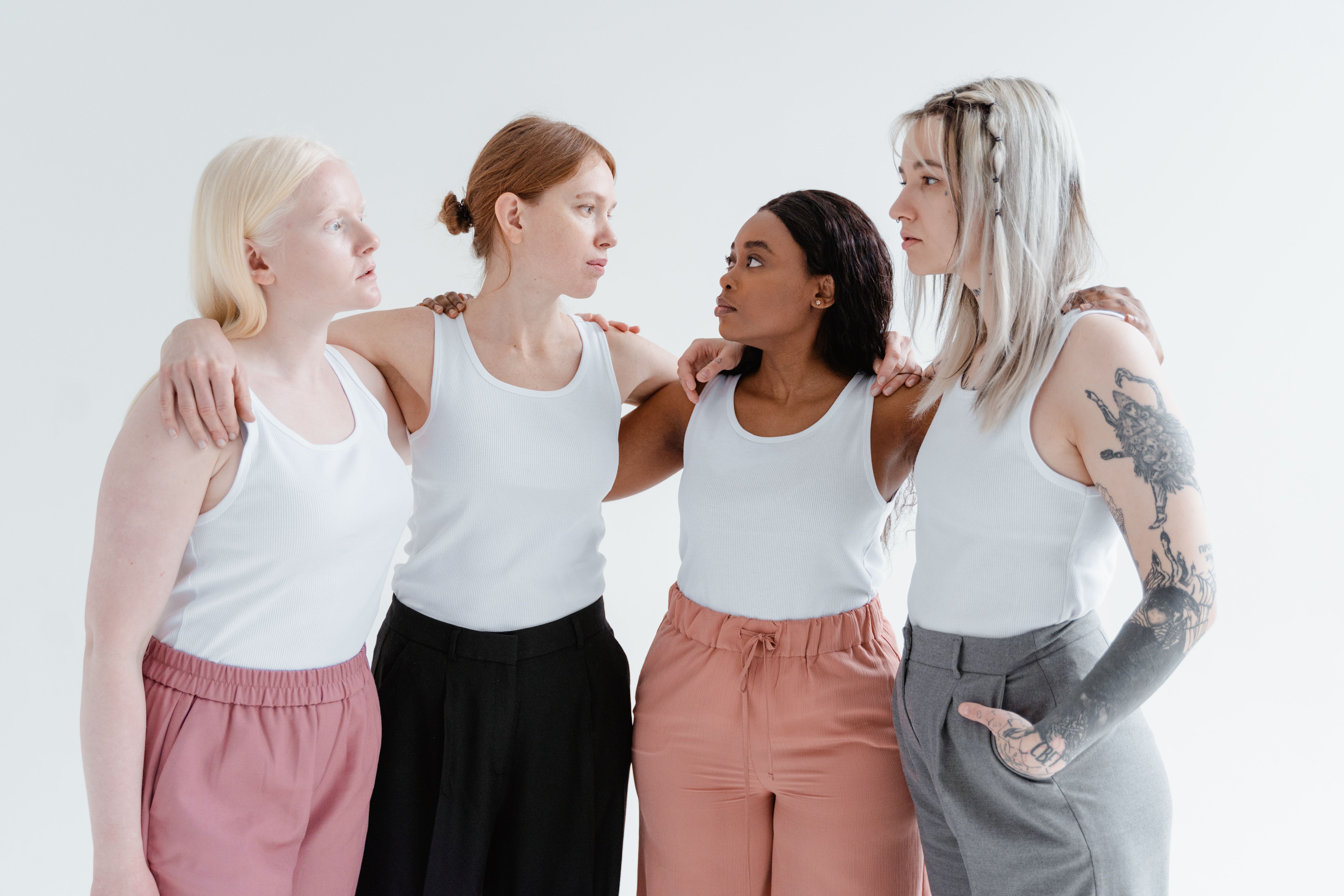 Four diverse young women embracing in a light-filled studio setting, promoting unity in diversity.